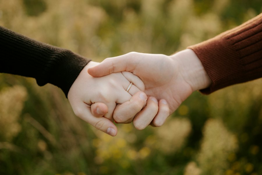 Duas mãos dadas, uma delas com aliança, sobre um fundo suave de campo